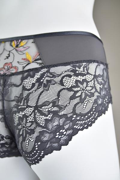 Biustonosz miękki  z fiszbinami.
Miseczki z beżowej siatki, na którą naszyty jest wzorzysty plen-motyw kwiatowy na grafitowym podkładzie.
Boczki z mikrofibry-wzmocnione fiszbiną, grafitowe ramiączka, bawet z koronki, środek zdobi zółta kokardka.
Pewna i sprawdzona konstrukcja z modelu Deziro dedykowana dla średnichi dużych biustów.
Skład surowcowy: 85%Poliamid, 10% Elastan, 5%Poliester.
 