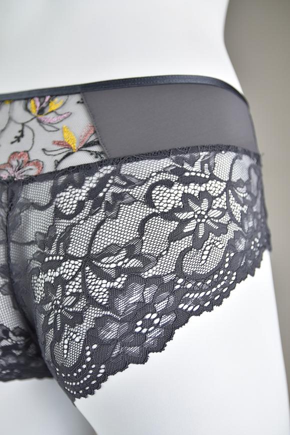 Biustonosz miękki  z fiszbinami.
Miseczki z beżowej siatki, na którą naszyty jest wzorzysty plen-motyw kwiatowy na grafitowym podkładzie.
Boczki z mikrofibry-wzmocnione fiszbiną, grafitowe ramiączka, bawet z koronki, środek zdobi zółta kokardka.
Pewna i sprawdzona konstrukcja z modelu Deziro dedykowana dla średnichi dużych biustów.
Skład surowcowy: 85%Poliamid, 10% Elastan, 5%Poliester.
 