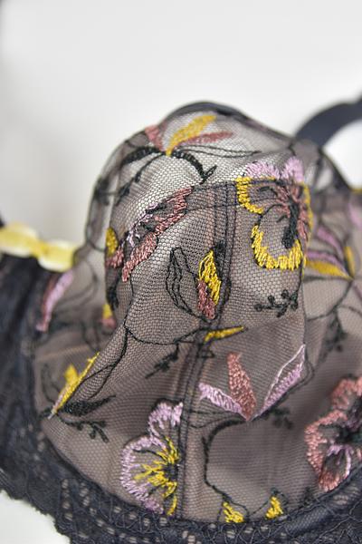 Biustonosz miękki  z fiszbinami.
Miseczki z beżowej siatki, na którą naszyty jest wzorzysty plen-motyw kwiatowy na grafitowym podkładzie.
Boczki z mikrofibry-wzmocnione fiszbiną, grafitowe ramiączka, bawet z koronki, środek zdobi zółta kokardka.
Pewna i sprawdzona konstrukcja z modelu Deziro dedykowana dla średnichi dużych biustów.
Skład surowcowy: 85%Poliamid, 10% Elastan, 5%Poliester.
 