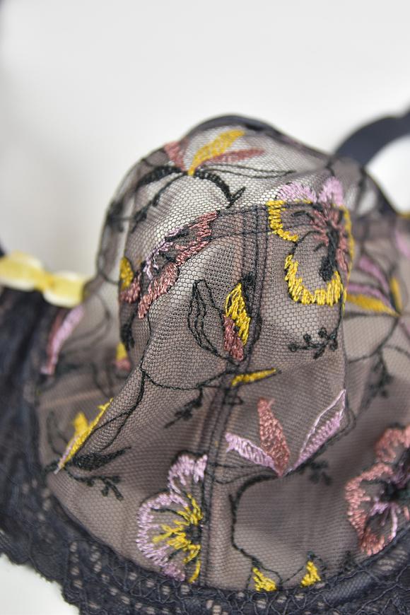 Biustonosz miękki  z fiszbinami.
Miseczki z beżowej siatki, na którą naszyty jest wzorzysty plen-motyw kwiatowy na grafitowym podkładzie.
Boczki z mikrofibry-wzmocnione fiszbiną, grafitowe ramiączka, bawet z koronki, środek zdobi zółta kokardka.
Pewna i sprawdzona konstrukcja z modelu Deziro dedykowana dla średnichi dużych biustów.
Skład surowcowy: 85%Poliamid, 10% Elastan, 5%Poliester.
 